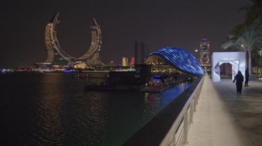 Lusail City 'deki Lusail marinası, Katar gece görüşü Lusail siluetini, gezinti güvertesinde yürüyen insanlarla birlikte Katara Kuleleri projesini gösteriyor.