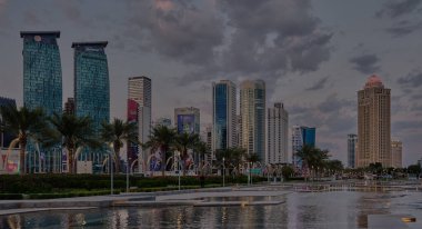 Doha, Katar-18 Kasım 2025: Doha, Katar Skyline, Sheraton parkından gün ışığı görüntüsü, suda yansıma ve arka planda bulutlar