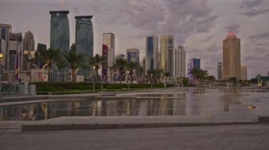 Doha, Katar - 2 Şubat 2024: Batı Körfezi 'nde Doha ufuk çizgisi günbatımı Otelin parkından çekilen ön planda yapay göl ve arka planda bulutlar