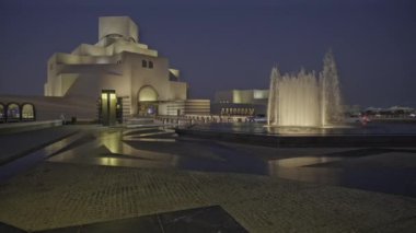 Doha, Katar - 11 Mart 2024: Katar İslami Sanat Doha Müzesi, Katar dış çekim ön planda fıskiyeyi ve arka planda müzenin ana girişini arabalarla ve yürüyen insanlarla gösteren alacakaranlık görüntüsü