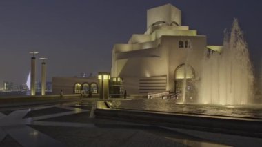 Doha, Katar - 11 Mart 2024: Katar İslami Sanat Doha Müzesi, Katar dış çekim ön planda fıskiyeyi ve arka planda müzenin ana girişini arabalarla ve yürüyen insanlarla gösteren alacakaranlık görüntüsü