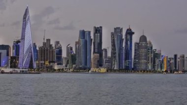 Doha, Katar-4 Mayıs 2024: Doha Katar gün batımında Corniche gezinti güvertesinden Katar bayrağıyla Arap körfezindeki darı gösteren silueti