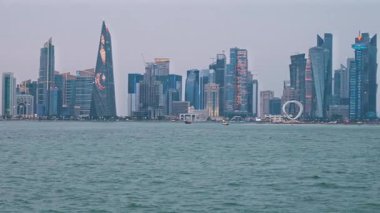 Doha, Katar-20 Nisan 2025: Katar bayrağıyla Arap körfezinde dhows 'u gösteren Corniche gezinti günbatımından Doha Katar silueti