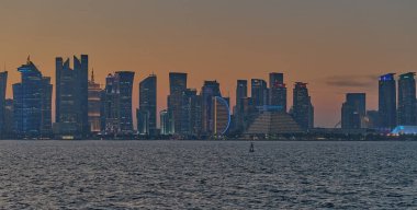 Doha, Katar-22 Nisan 2025: Katar bayrağıyla Arap körfezinde dhows 'u gösteren Corniche gezinti günbatımından Doha Katar silueti