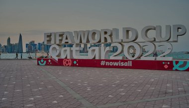 Doha, Katar-20 Nisan 2025: Doha corniche FIFA Dünya Kupası Katar 2022 tabelasını gösterirken, insanlar yürüyor ve Doha silueti arka planda