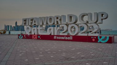 Doha, Katar-20 Nisan 2025: Doha corniche FIFA Dünya Kupası Katar 2022 tabelasını gösterirken, insanlar yürüyor ve Doha silueti arka planda