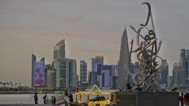 Doha, Katar-20 Nisan 2025: Kaligrafi Heykeli 'ni ve Katar bayrağıyla Arap Körfezi' nde çizimleri gösteren Corniche gezinti günbatımından Doha Katar silueti