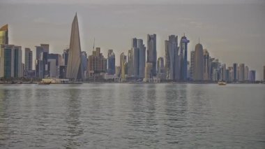 Doha, Katar-25 Nisan 2025: Katar bayrağıyla Arap körfezinde dhows 'u gösteren Corniche gezinti günbatımından Doha Katar silueti