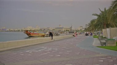 Doha, Katar-20 Nisan 2025: Katar bayrağıyla Arap körfezinde dhows 'u gösteren Corniche gezinti günbatımından Doha Katar silueti
