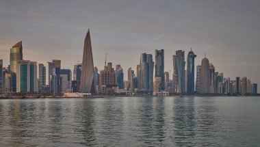 Doha, Katar-22 Nisan 2025: Katar bayrağıyla Arap körfezinde dhows 'u gösteren Corniche gezinti günbatımından Doha Katar silueti