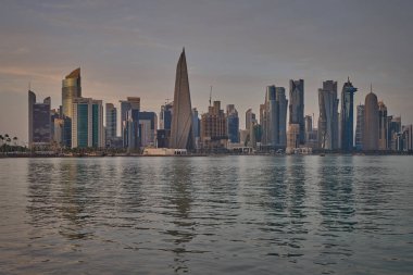 Doha, Katar-22 Nisan 2025: Katar bayrağıyla Arap körfezinde dhows 'u gösteren Corniche gezinti günbatımından Doha Katar silueti