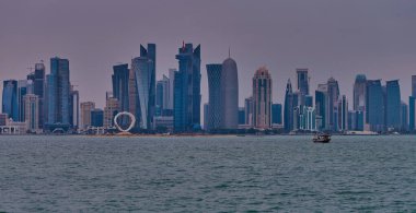 Doha, Katar-22 Nisan 2025: Katar bayrağıyla Arap körfezinde dhows 'u gösteren Corniche gezinti günbatımından Doha Katar silueti