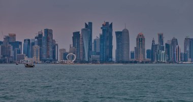 Doha, Katar-22 Nisan 2025: Katar bayrağıyla Arap körfezinde dhows 'u gösteren Corniche gezinti günbatımından Doha Katar silueti