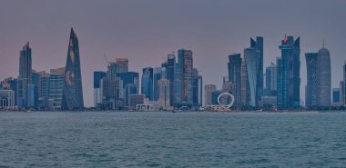 Doha, Katar-22 Nisan 2025: Katar bayrağıyla Arap körfezinde dhows 'u gösteren Corniche gezinti günbatımından Doha Katar silueti