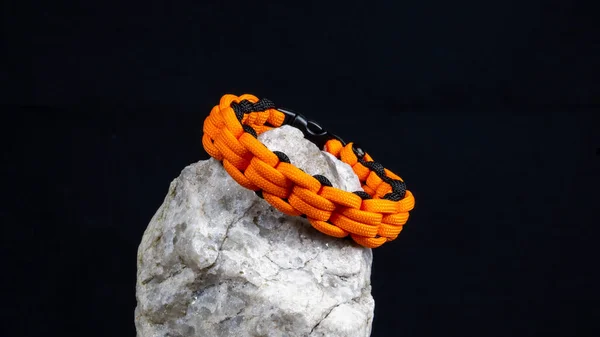 stock image Braided paracord bracelet on a stone, on a black background. Handmade, creative design.