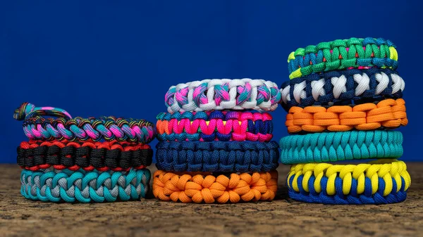 Mavi arka planda örülmüş bir sürü paraşüt bilekliği var. El yapımı, yaratıcı tasarım.