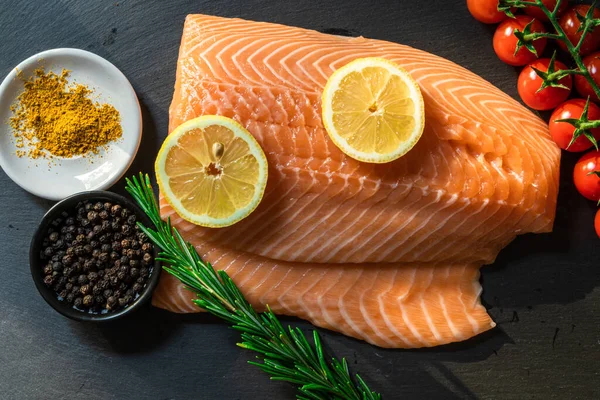 Koyu taştan bir arka planda baharatlı taze somon balığı bifteği. Tuz, baharat, baharat ve diğer malzemeler..