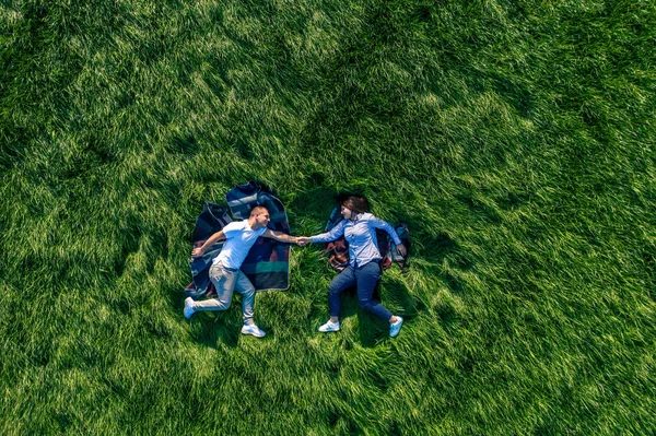 Parktaki büyük yeşil bir çayırda birbirine aşık bir çift. Mutluluk ve sükunetin drone görüntüsü.