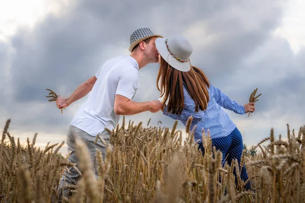 A couple in love enjoys relaxing in a wheat field. Romantic couple kissing in a moment of love in a golden wheat field. The concept of people, lifestyle, travel, nature and recreation.