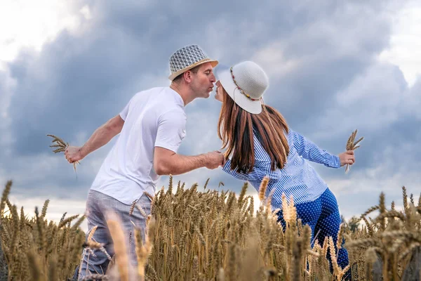 A couple in love enjoys relaxing in a wheat field. Romantic couple kissing in a moment of love in a golden wheat field. The concept of people, lifestyle, travel, nature and recreation.