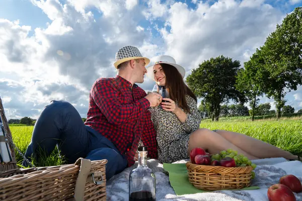 Loving couple at a picnic in the park. Wine and fruit in a wicker basket. A wonderful evening spent in nature.