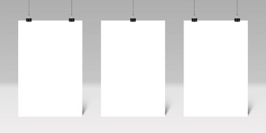Gri bir duvardaki klasör kliplerinden sarkan üç boş dikey poster sanat eserlerini veya tasarımları göstermek için ideal bir ortam oluşturur, yaratıcı bir ortam veya sunum alanı oluşturur.