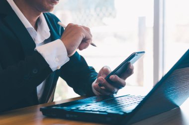 İş adamları ofislerdeki masalarda çalışmak için cep telefonu ve dizüstü bilgisayar kullanıyorlar..