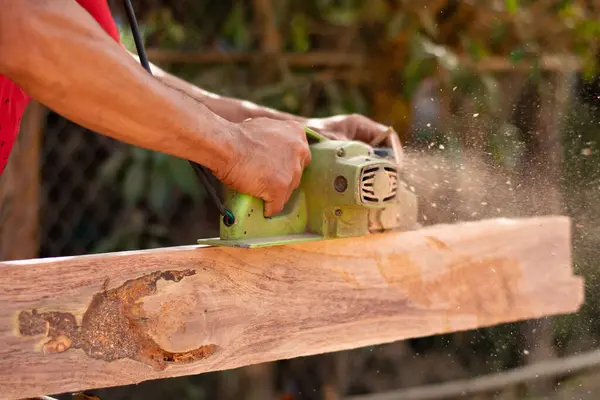 stock image Homebuilder is using a planer to make furniture, preparing materials for home repair work. Side view.