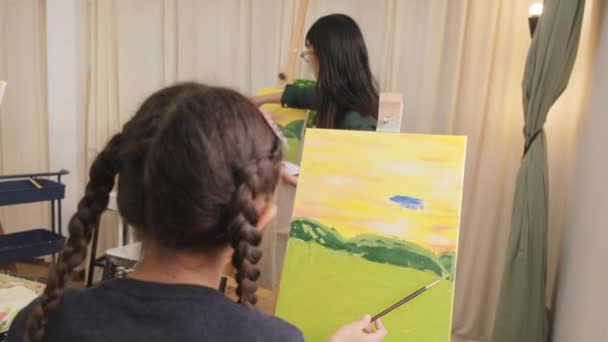 亚洲女教师在艺术课的画布上向小女孩讲授丙烯酸彩绘 在小学演播室教育中创造性地学习技巧 — 图库视频影像