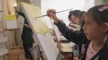 Küçük bir kız, sanat sınıfındaki çok ırklı çocuklarla akrilik renkli resim yapmaya odaklanır. İlkokulda atölye eğitiminde yetenek ve beceri sahibi yaratıcı öğrenme..