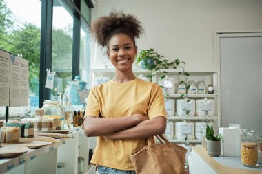 Yeniden kullanılabilir bir alışveriş çantası ile genç Afrikalı Amerikalı kadın müşterinin portresi. Doldurucu mağazada mutlu gülümsemeler, sıfır atık perakende market, ve plastiksiz, çevre dostu, sürdürülebilir yaşam tarzı..
