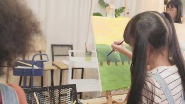 アジアの少女は 教室で多人種の子供たちとキャンバス上のアクリル色絵具に焦点を当て 小学校のスタジオ教育で才能とスキルを持つ創造的な学習 — ストック動画