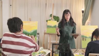 Asyalı bir bayan öğretmen, sanat sınıfındaki akrilik renkli tuvale resim çizmeyi öğretiyor ve ilkokul stüdyo eğitiminde yaratıcı bir şekilde öğreniyor..