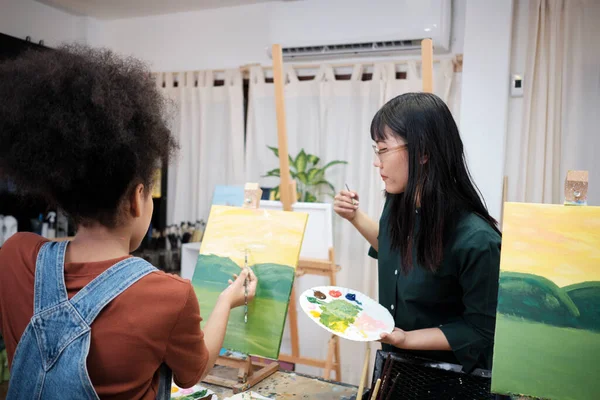 アジアの女性教師は 芸術教室でキャンバス上のアクリルカラー絵具の学生の女の子に教え 実証し 創造的に小学校のスタジオ教育でスキルで学ぶ — ストック写真