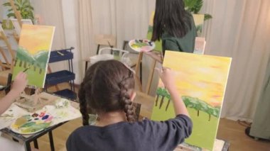 Küçük kız, resim sehpasında resim yapmaya odaklanır. Sanat sınıfındaki öğretmenler ve çocuklarla birlikte. İlkokulda atölye eğitiminde yetenek ve beceri gerektiren yaratıcı öğrenme..