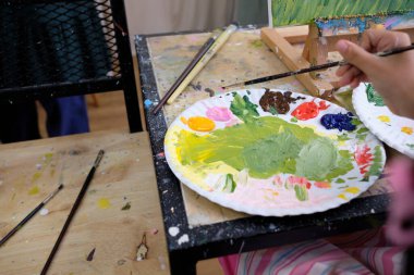 Yakın çekim, akrilik renk paleti, sanatçının eliyle bir resim hazırlamak ve boyamak, tuval içinde canlı çok renkli resim, resim sehpası ile renkli yaratıcılık, yetenek becerileri, sanatsal hayal gücü tasarımı.