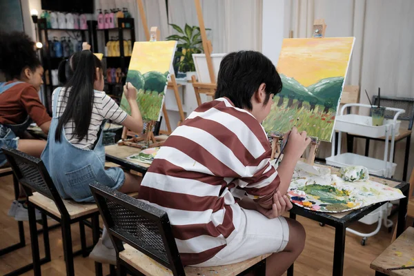 A group of student kids concentrates on acrylic color picture painting with a paintbrush on canvas in art classroom, creatively learning with talents and skills at elementary school studio education.