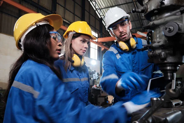 一个穿着保护和安全制服和安全帽的工业工人团队 男性经理和女性同事在制造业工厂与金属加工机械一起工作 专业生产工程师 图库图片