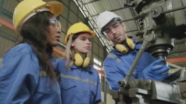 Koruyucu ve güvenlik üniformaları ve şapka giyen bir endüstri işçileri ekibi, erkek yönetici ve bayan meslektaşlar fabrikada metal fabrikalarında çalışıyor. Profesyonel üretim mühendisi.