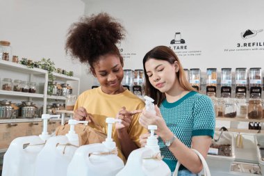 İki bayan müşteri, sıfır atık ve yeniden doldurma mağazalarında geri dönüşümlü şişeleri olan doğal organik ürünlerle alışveriş yapmaktan, çevre dostu bakkallardan ve sürdürülebilir perakendecilerden memnun ve mutlular..