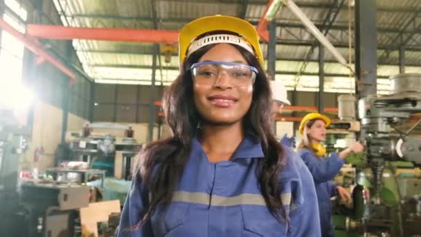 身着防护服 头戴安全帽 面带微笑地看着相机的黑人职业女性员工的画像 工程师们在她身后的一家金属制品制造厂工作 — 图库视频影像