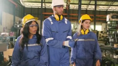 Koruyucu ve güvenlik üniformaları ve kasketleri olan bir endüstri işçileri ekibi, erkek müdür ve iş arkadaşları fabrikada yürüyen ve metal işleri tartışıyorlar. Profesyonel üretim mühendisi.