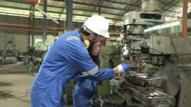 Koruyucu ve güvenlik üniforması ve şapka giyen iki sanayi işçisi, erkek müdür ve siyah meslektaşı fabrikada metal fabrikalarında çalışıyor. Profesyonel üretim mühendisi ekibi..