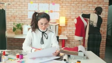 Asyalı orta yaşlı kadın moda tasarımcısı genç bir terziye renkli iplik ve elbise koleksiyonu fikirleri için dikiş kumaşı, profesyonel butik küçük işletme eğitimi veriyor.. 