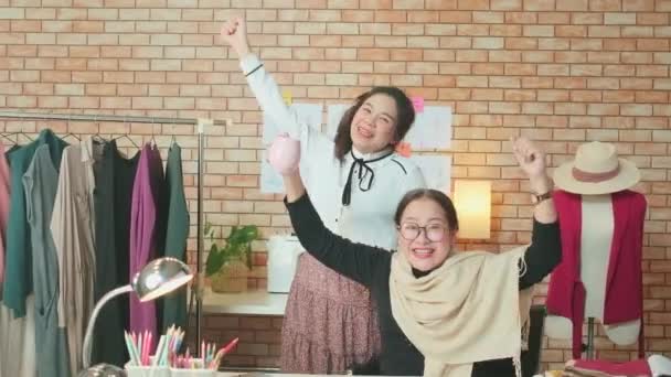 亚洲中年女性时装设计师和年轻的实习裁缝师庆祝服装设计工作的成功 并在造型师工作室满意 快乐的服装精品店小生意 — 图库视频影像