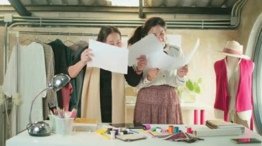 Asyalı orta yaşlı kadın moda tasarımcısı ve genç stajyer terzi kutlama yapıyor ve elbise tasarlama başarısı ile neşeli, atölyede iş kağıdı atıyor, mutlu kostüm butiği küçük iş yeri..