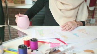 Kadın moda tasarımcısının elinin yakın plan fotoğrafı, kahve fincanı, kağıda çizim, elbise tasarımı koleksiyonu. Profesyonel butik kostüm terzisi ve yaratıcı stilist.. 