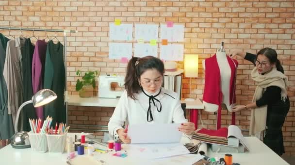 亚洲中年女性时装设计师在工作室教一位年轻的受训者裁缝用彩线和缝纫面料设计服装 专业精品小生意 — 图库视频影像