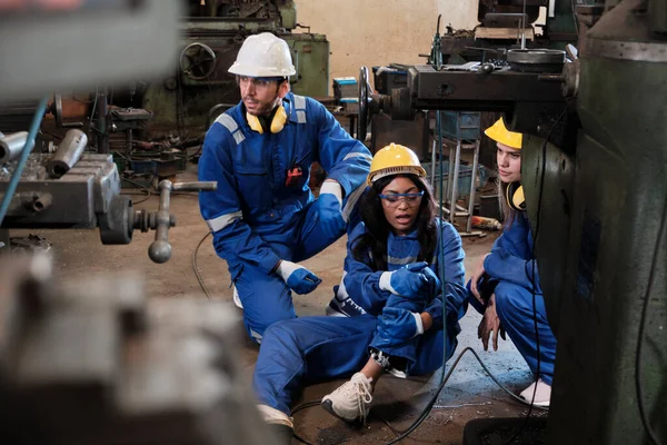 Painful accident in industrial production metalwork, African American female worker injured her leg, male engineer and colleague team helped first aid with care at manufacturing machinery factory.