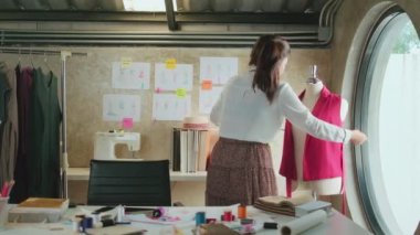 Asyalı genç bayan moda tasarımcısı, kukla şekillerini ölçerek ve dikiş, elbise tasarımı koleksiyonu ve profesyonel butik terziliği girişimcisi için yaratıcı fikirler çizerek stüdyoda çalışır.. 